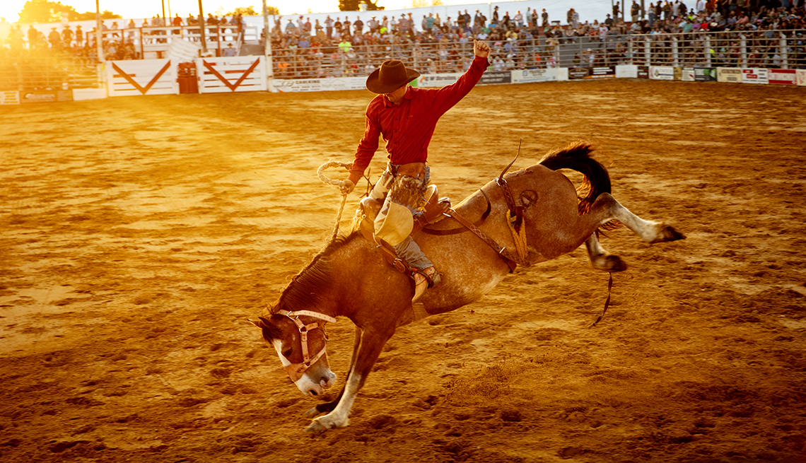 a horse tries to buck its its rider in a red shirt and cowboy hat at a rodeo