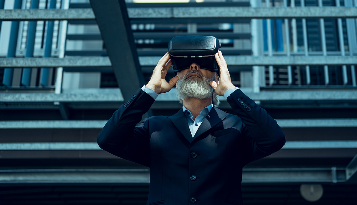 a man in a jacket and shirt looks into virtual reality goggles against a dark background