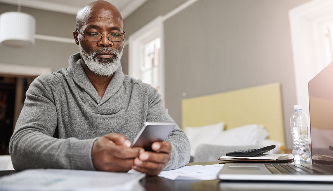 hombre sentado en su mesa mira su teléfono
