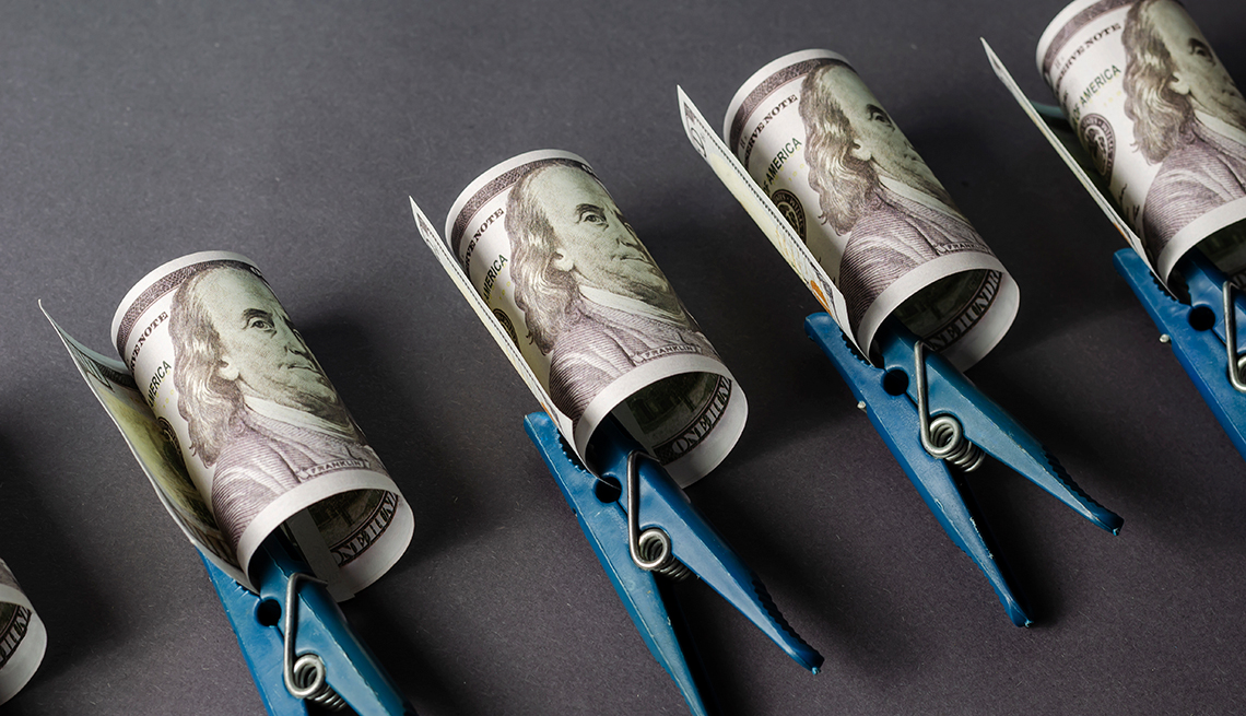 Fila de dólares enrollados y sostenidos con un gancho de ropa azul.   