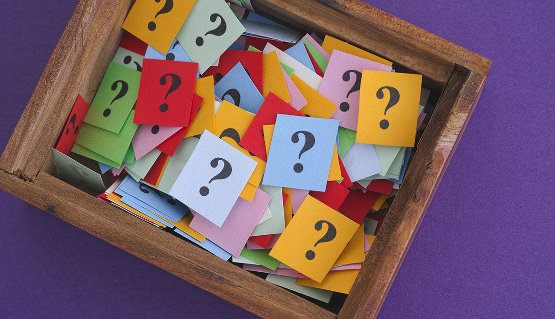 Caja de madera llena con papeles de colores que tienen un signo de interrogación