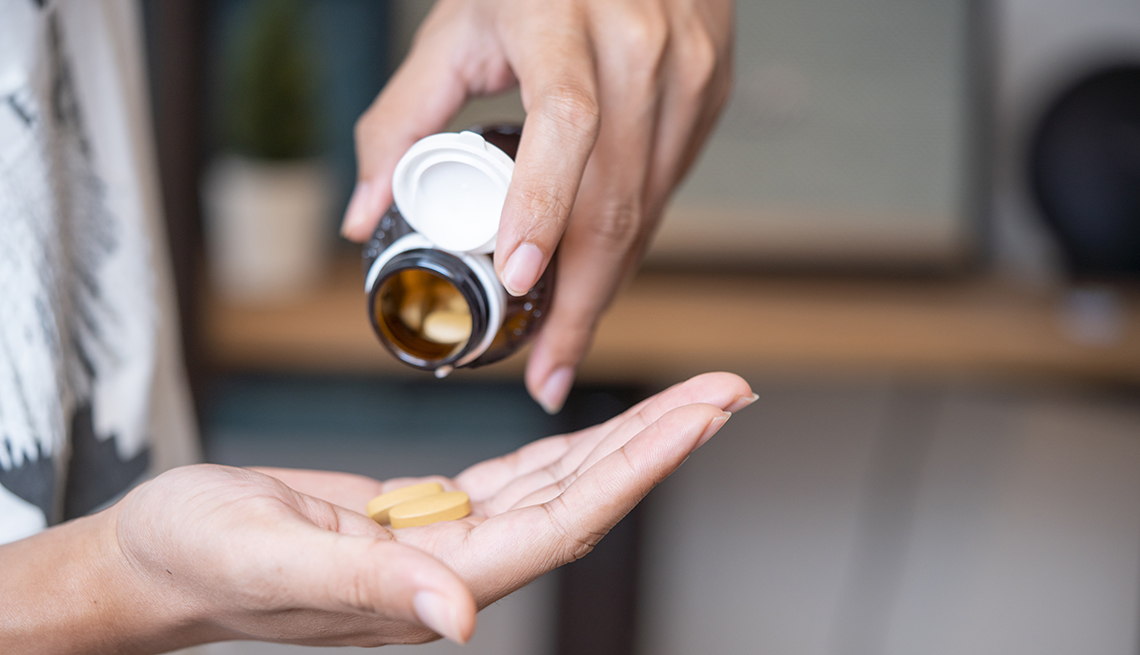 Una mujer vierte unas vitaminas en su mano desde un frasco