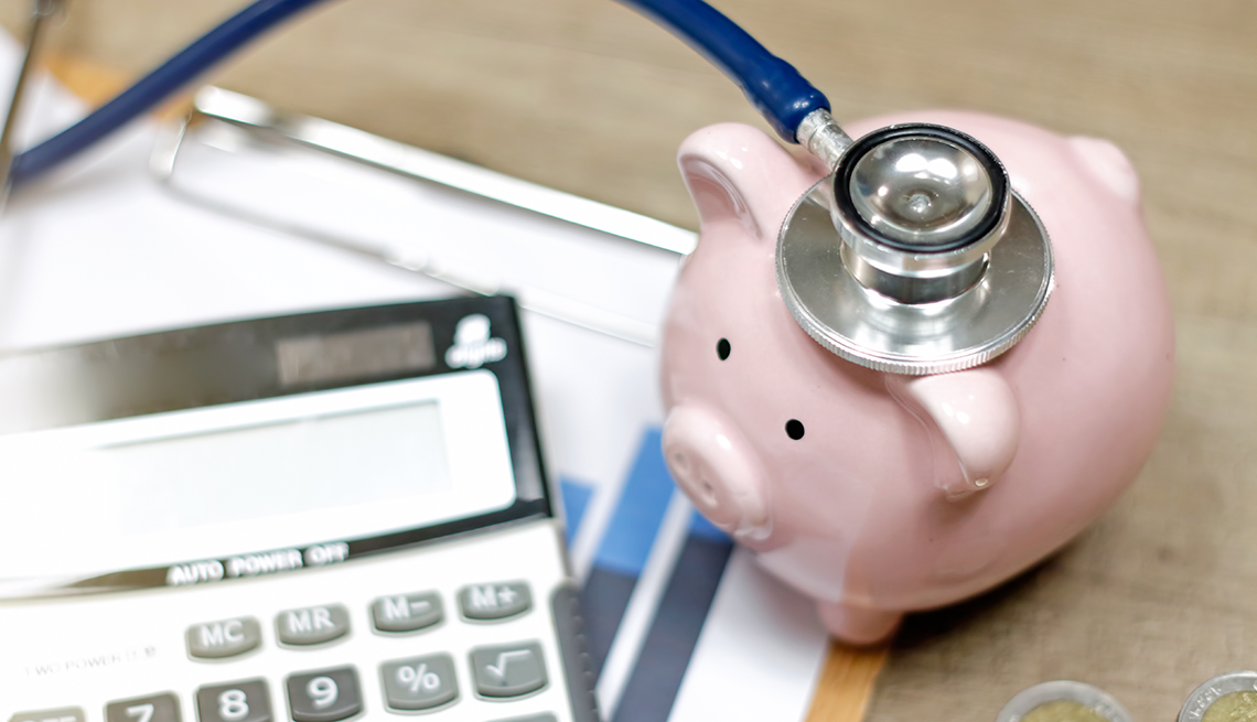 Un estetoscopio sobre una alcancía y una calculadora sobre una mesa