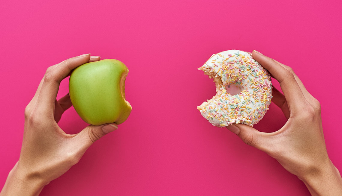 Dos manos, una sostiene una manzana y la otra una dona